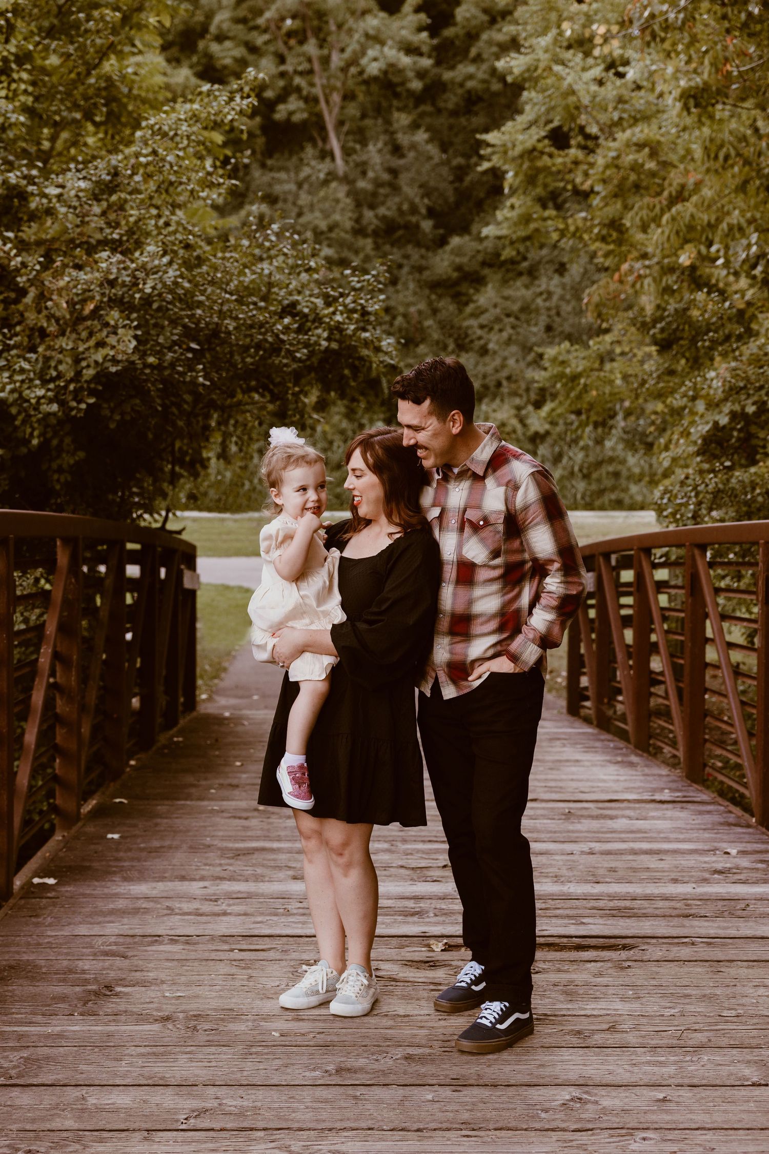 A family shares an intimate moment together while standing on a wooden bridge in a park.