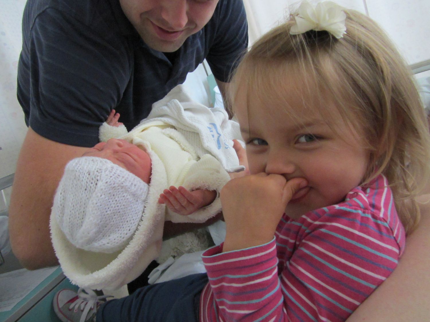 A candid family moment showing siblings meeting their newborn baby for the first time.