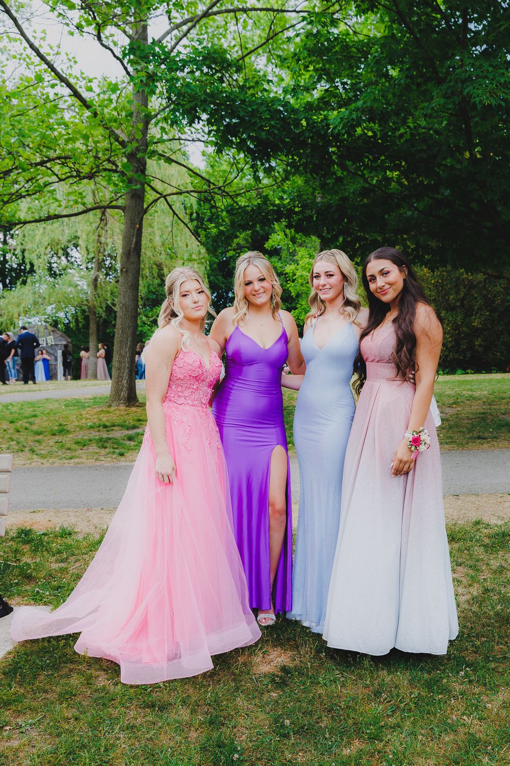 Four formal dresses in pink, purple, and pastel tones photographed in park setting.