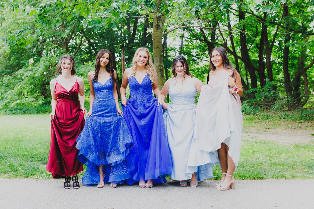 Group photo showing five formal dresses in red, blue, and neutral colors on outdoor path.