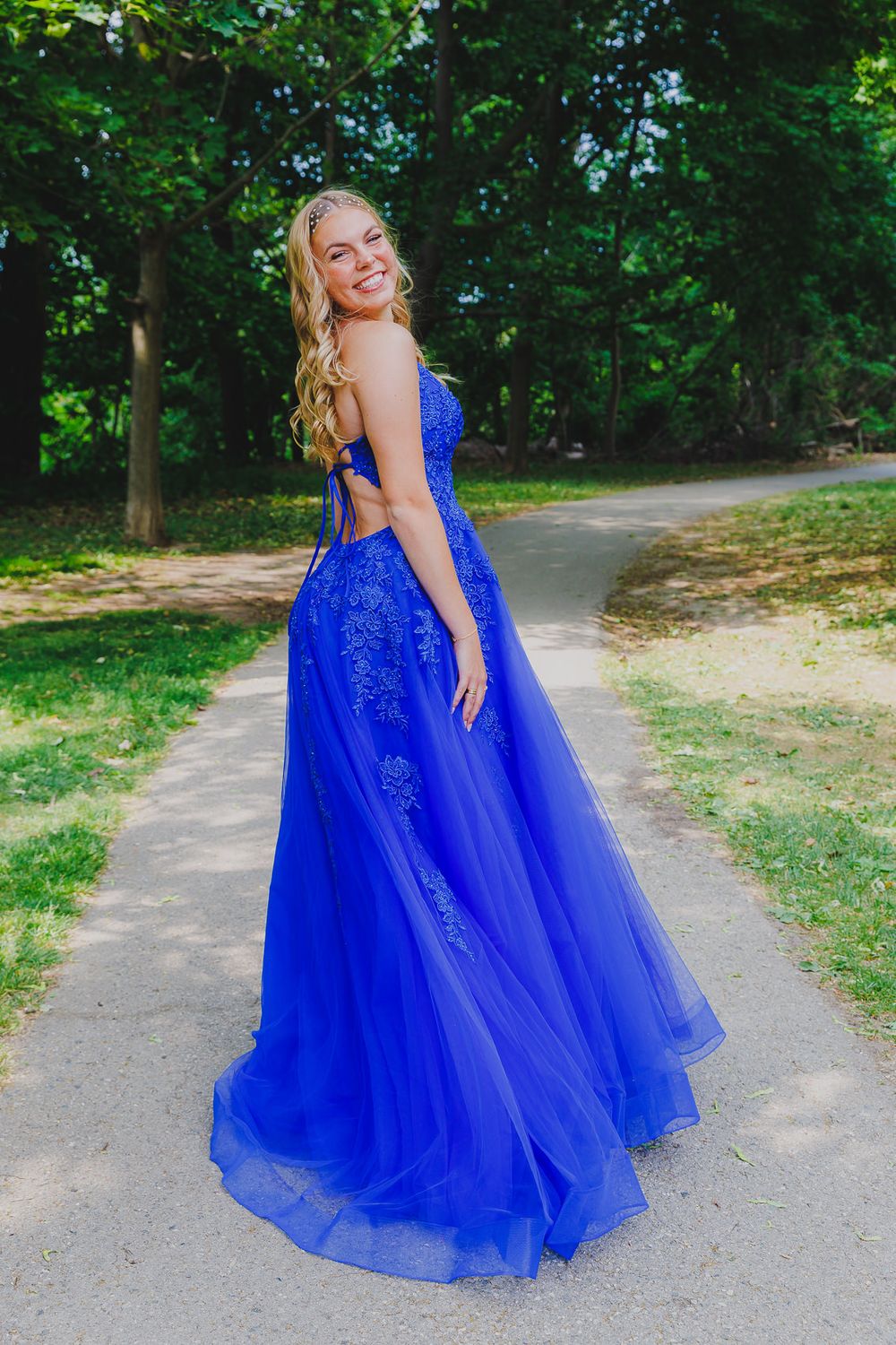 Sparkling royal blue ball gown with open back detail captured on garden pathway.