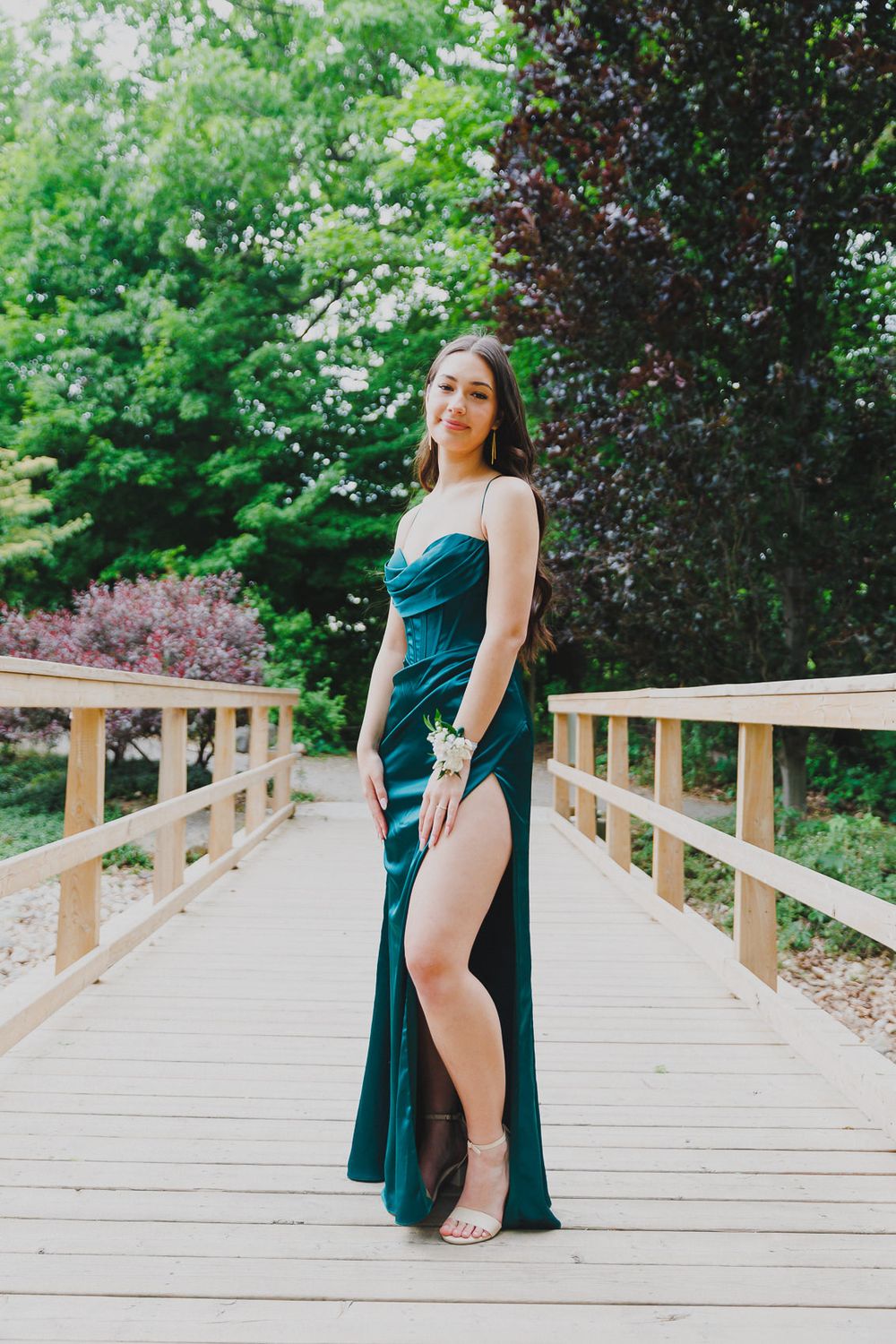 Stunning teal evening gown with thigh-high slit photographed on wooden bridge walkway.