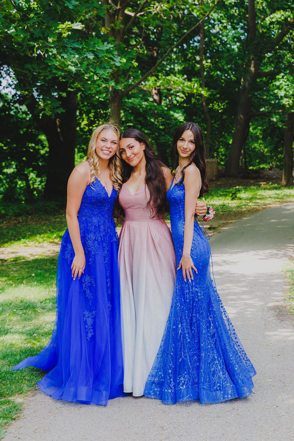 Three formal dresses in royal blue and pink photographed outdoors on park pathway.