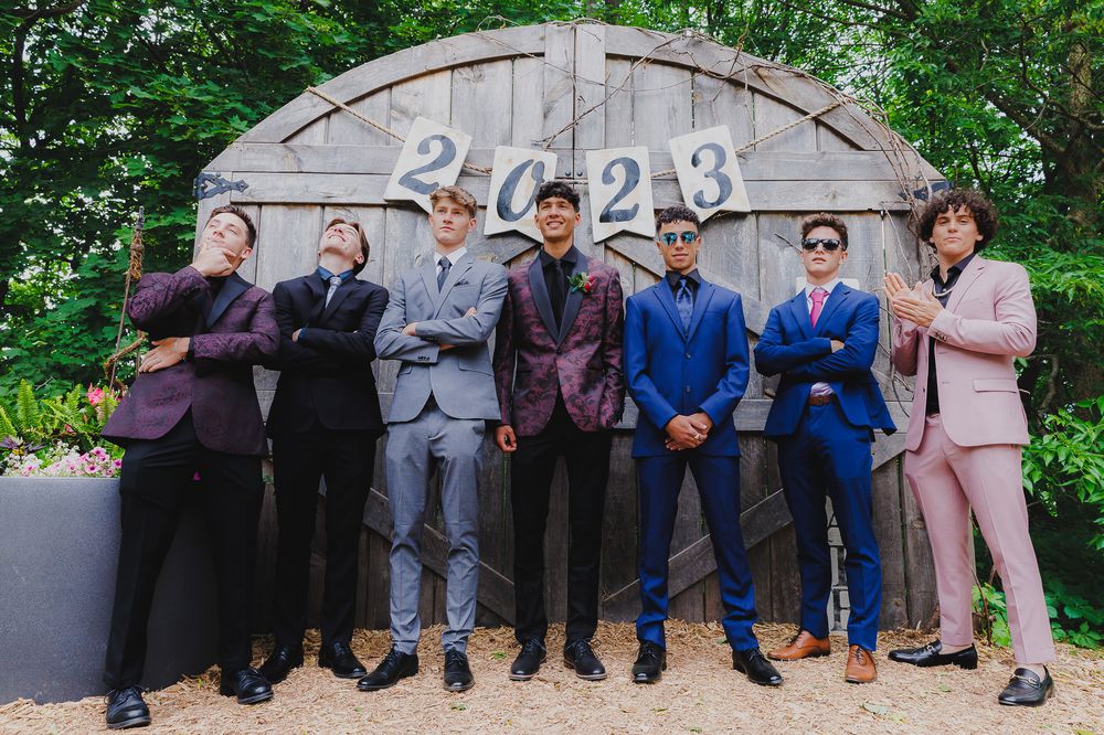 Group wearing colorful formal suits posing in front of curved stone wall with 2023 text.