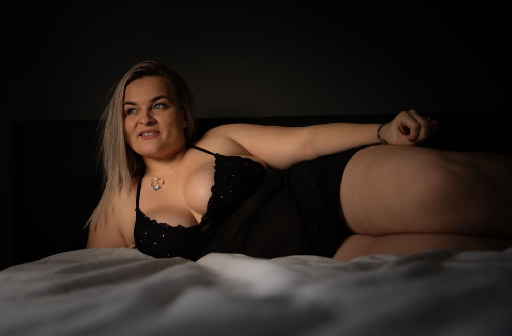 Boudoir photo featuring moody lighting and dark shadows on a bed with white linens.