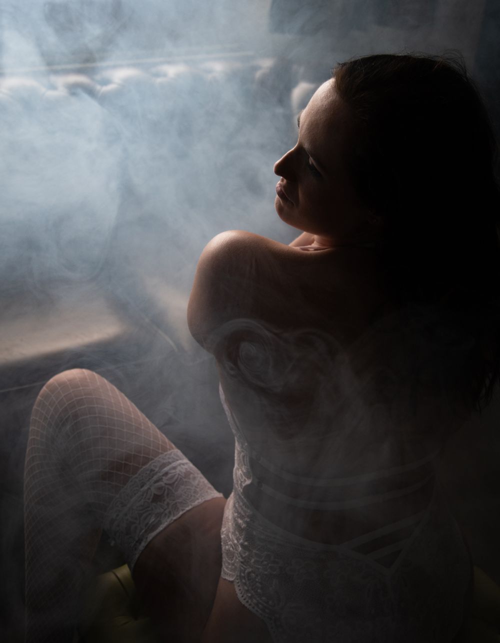 Ethereal portrait with smoke effects and white lace against moody lighting.