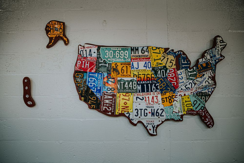 Creative map of United States made from vintage license plates mounted on white wall.