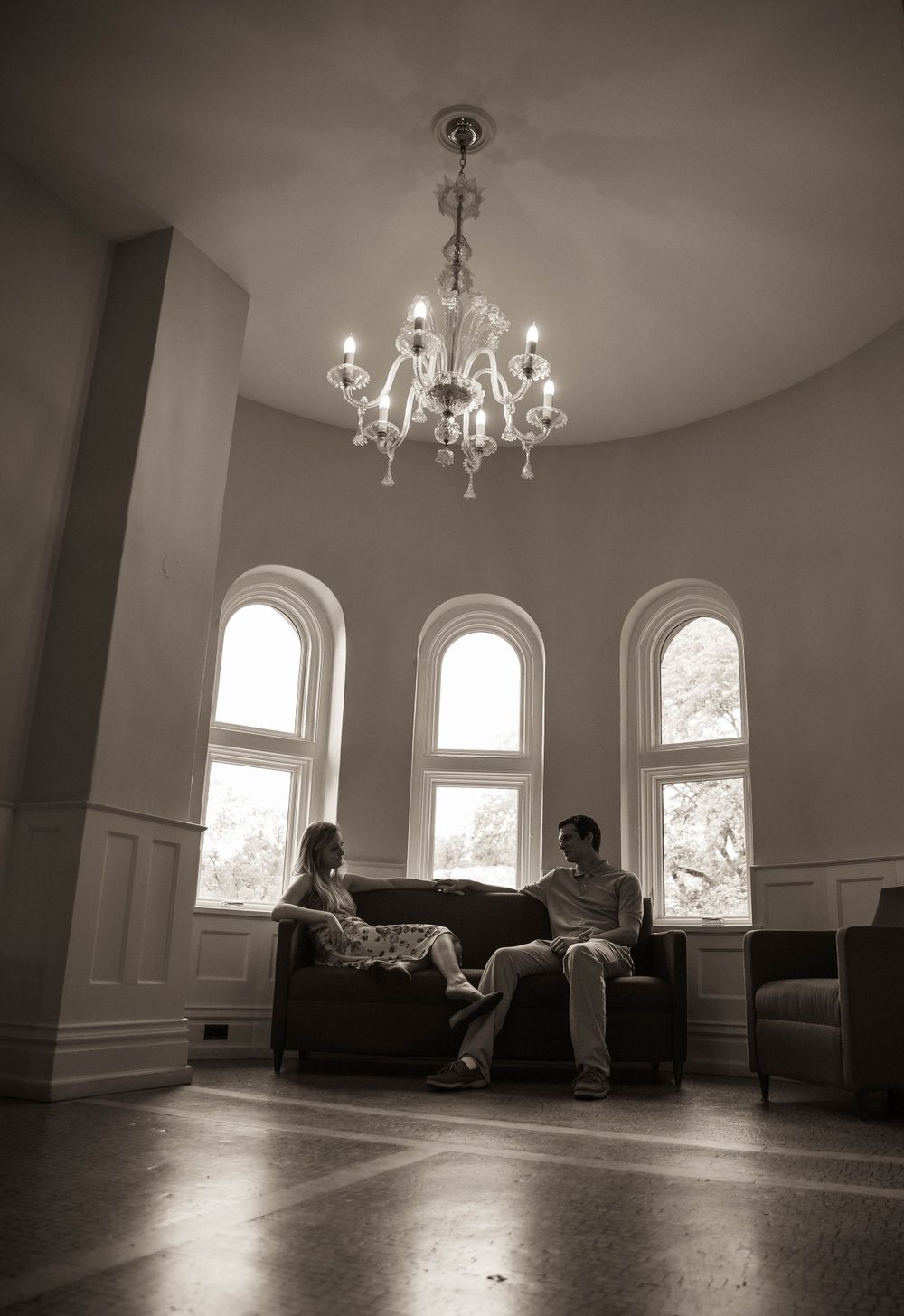 Elegant room with arched windows, crystal chandelier, and people relaxing on a sofa.