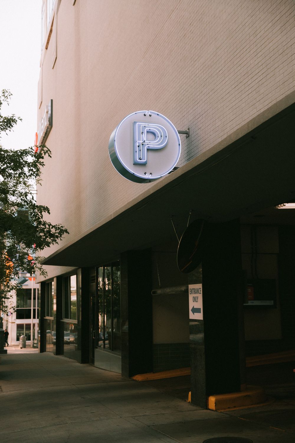 An illuminated letter P sign mounted on a beige building exterior with a black awning.