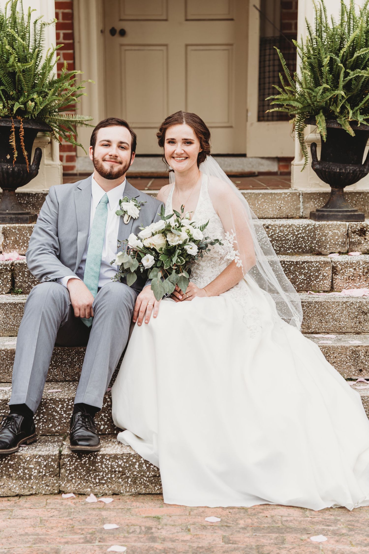 Elegant wedding portrait of couple seated on brick stairs with potted ferns.