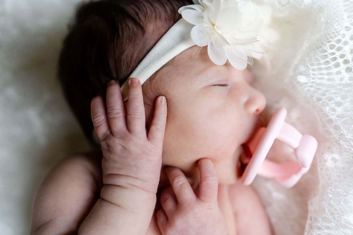 newborn girl with white floral headband and pink pacifier