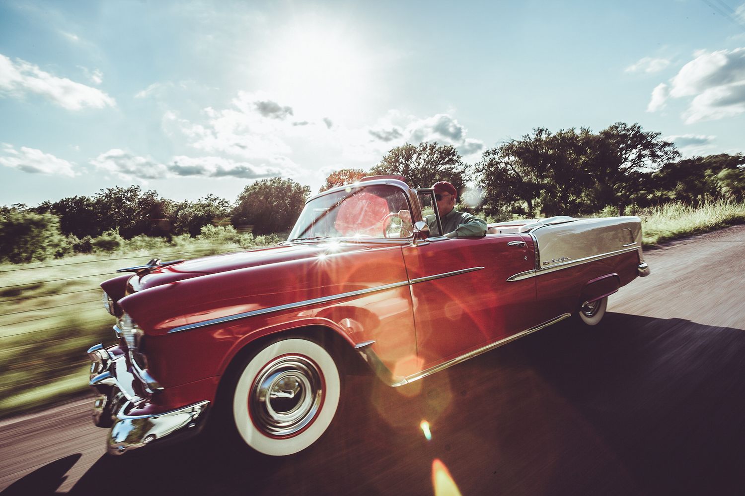 red vintage car racing down the road with sunflare