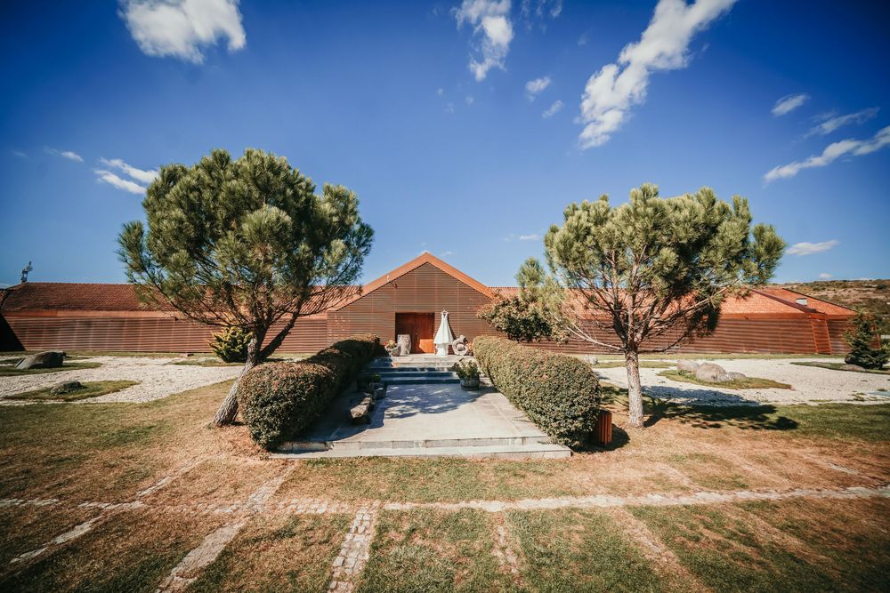 Small chapel with symmetrical trees and driveway under bright blue sky.