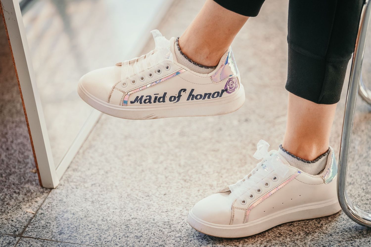 White sneakers with 'maid of honor' text written on the side against a light floor.