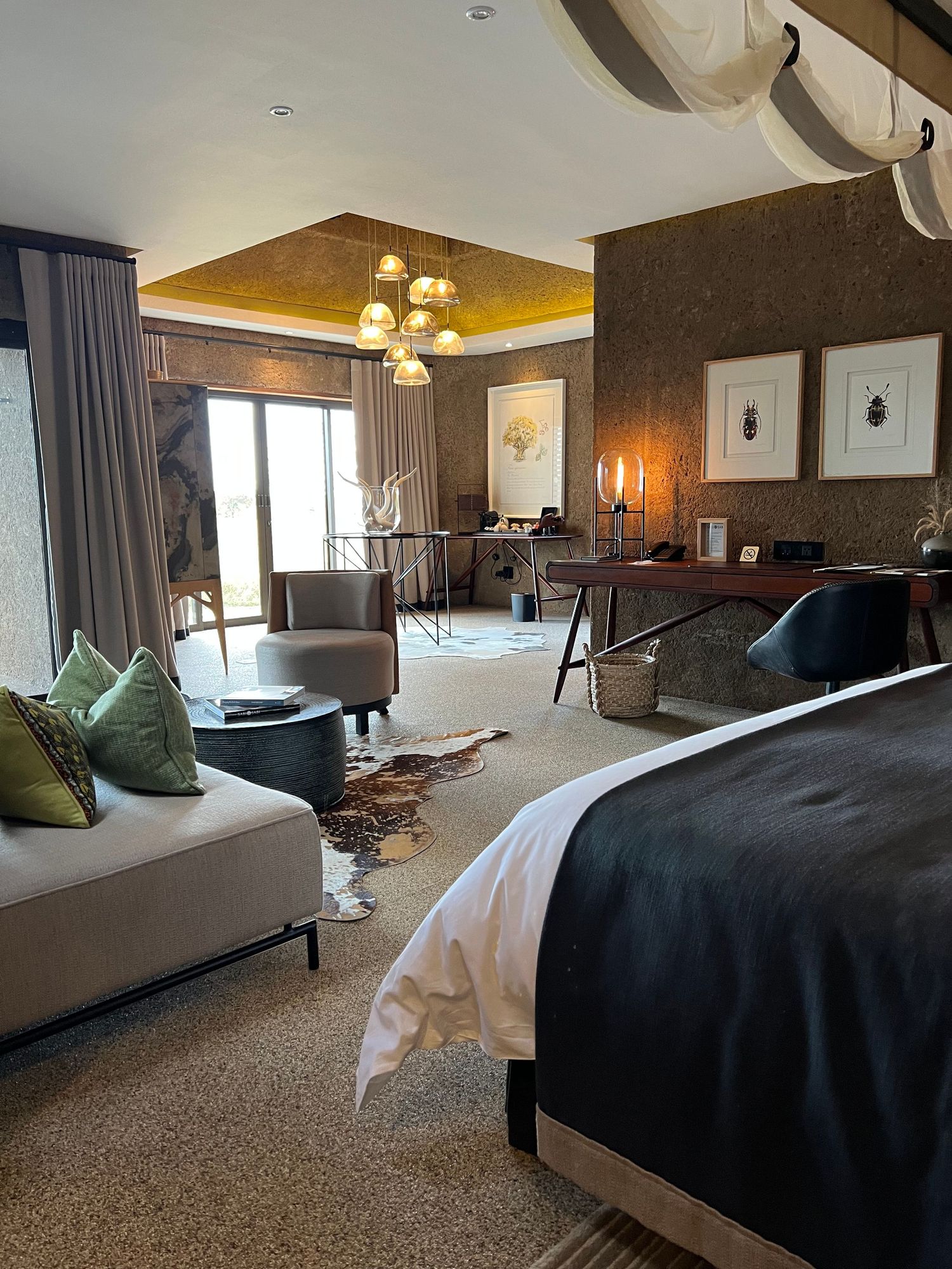 Luxurious hotel suite with modern decor, featuring a gold-accented ceiling and plush seating area.