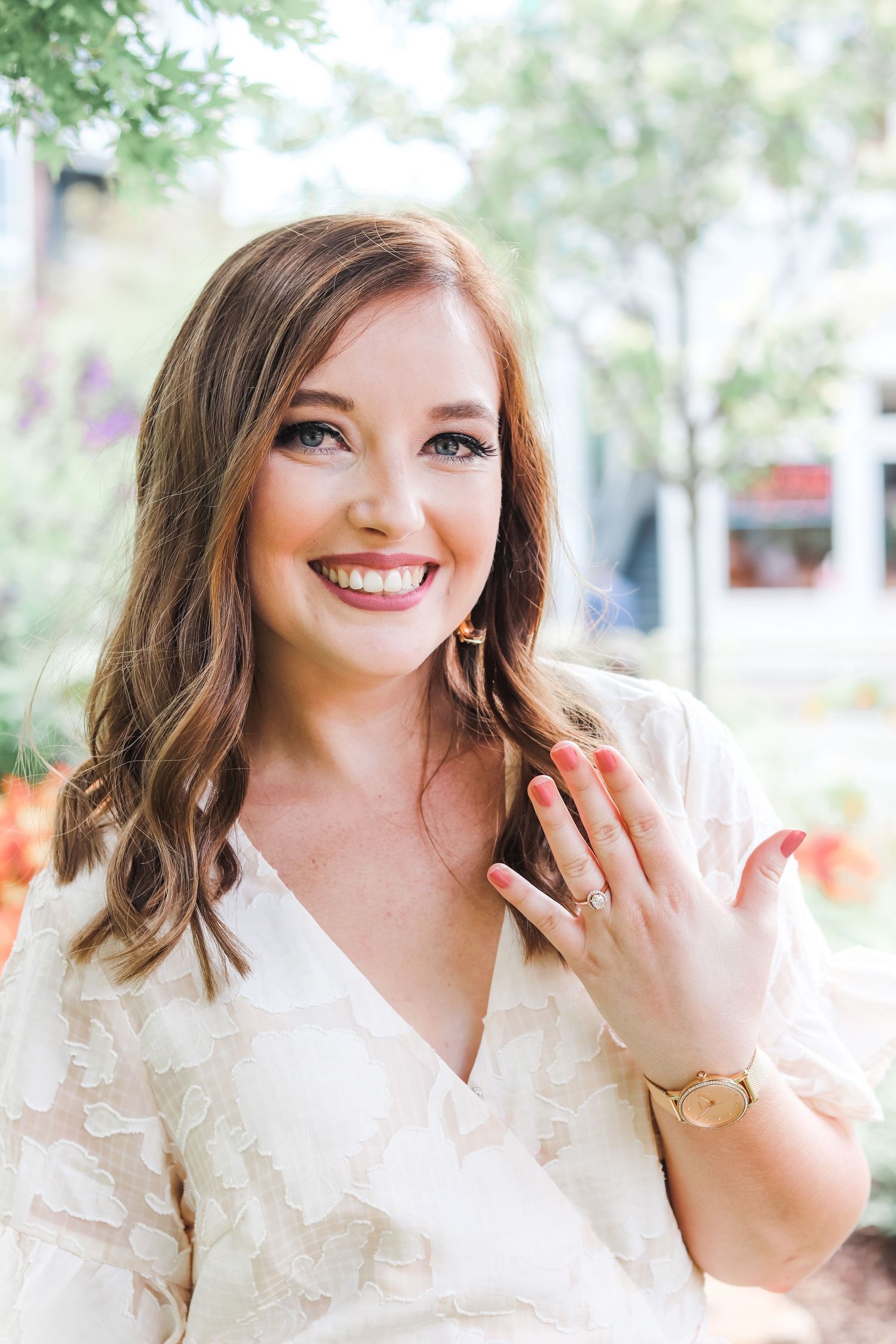 A person wearing a white ruffled top smiles warmly outdoors with trees in the background.