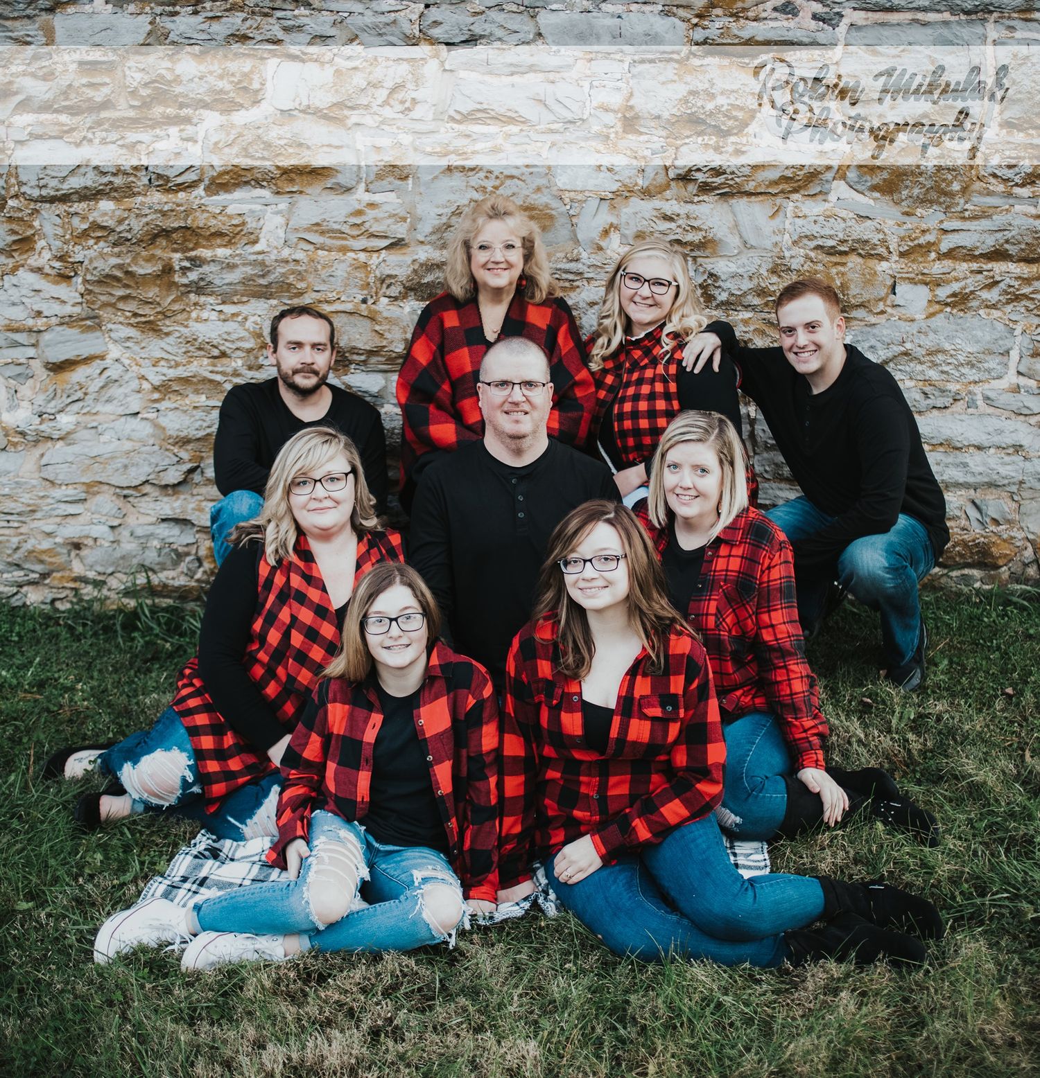 Family group wearing coordinated red buffalo plaid shirts pose together against a stone wall.