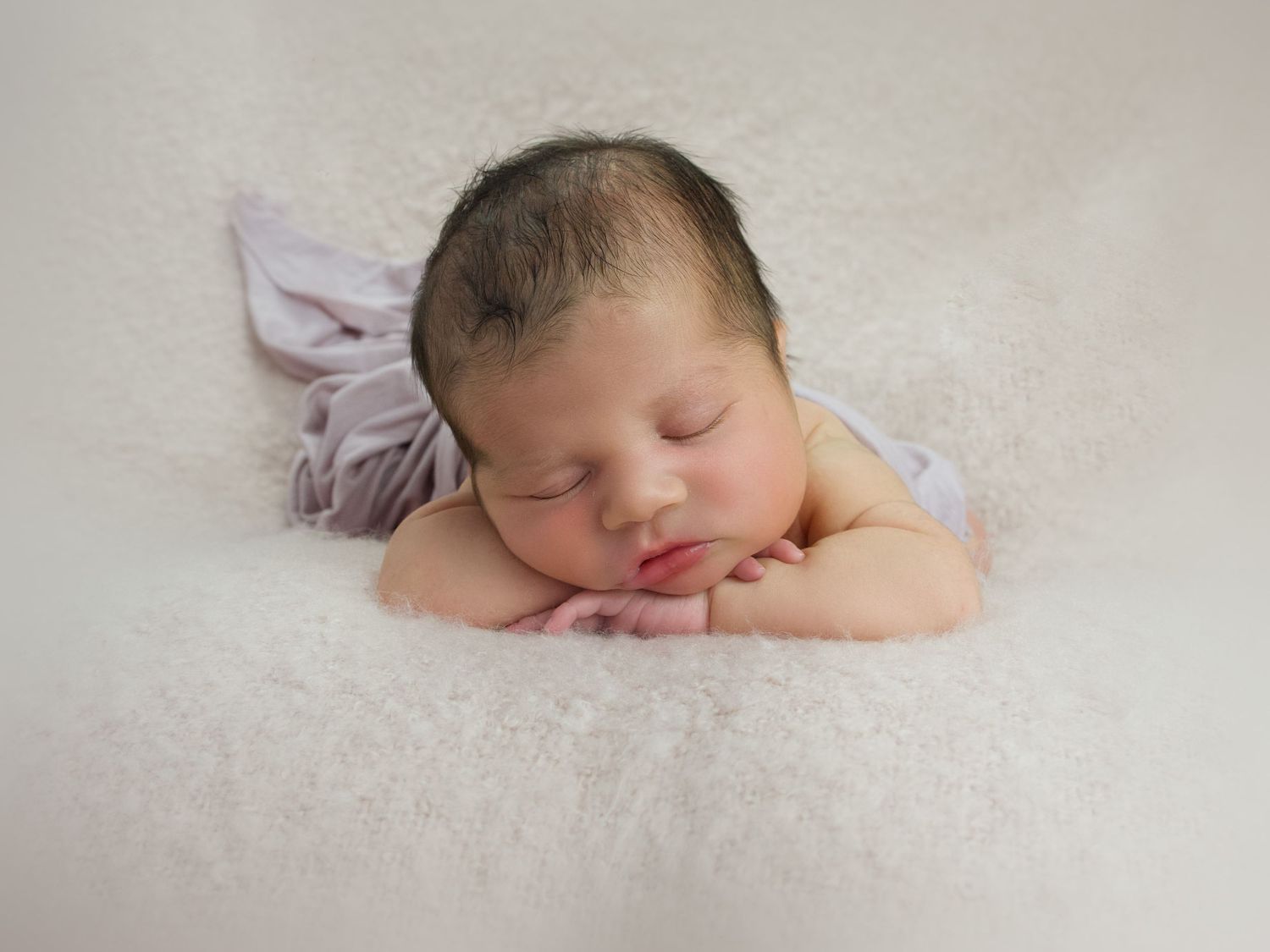newborn baby girl face forward with hands under chin lying on a pink blanket