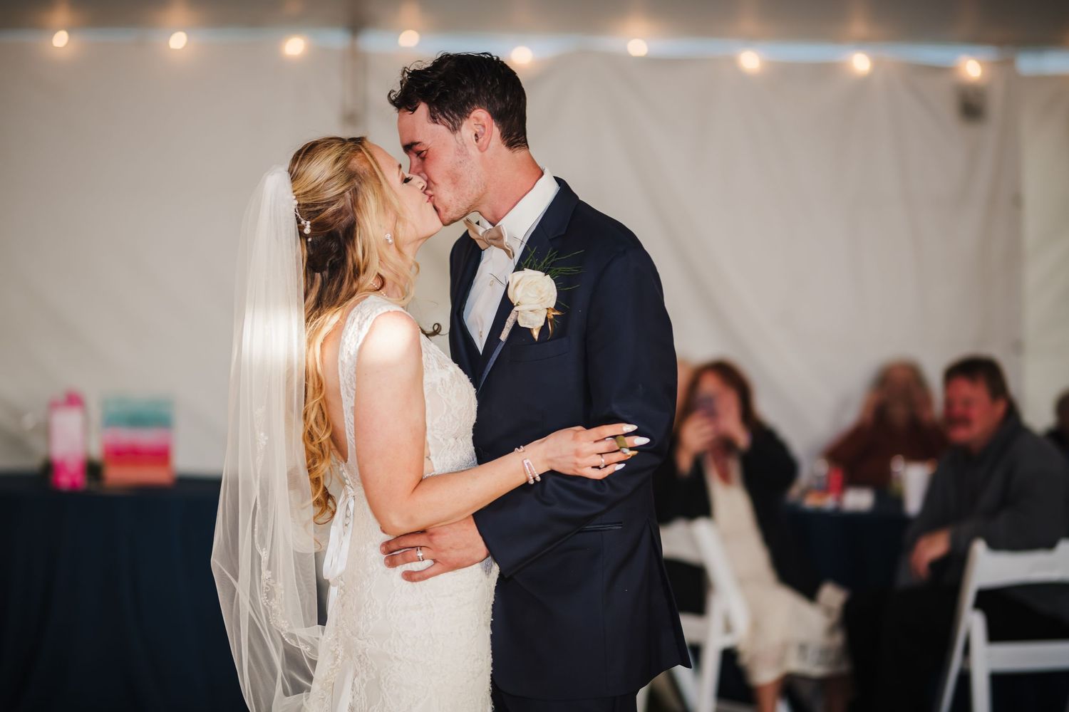 A romantic first dance moment between newlyweds at their wedding reception with guests in background.
