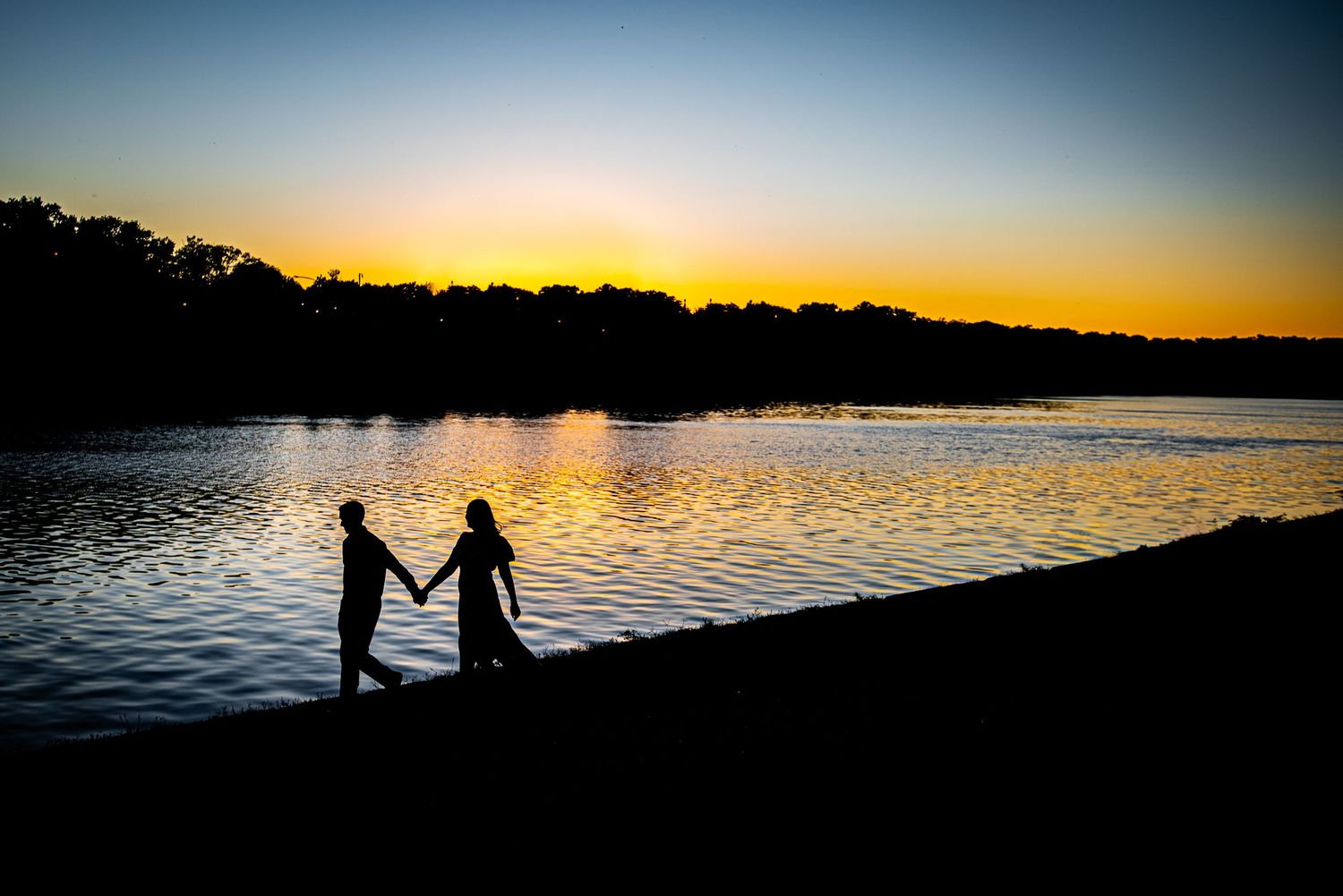 Silhouettes of two people holding hands against a golden sunset reflecting on calm waters.