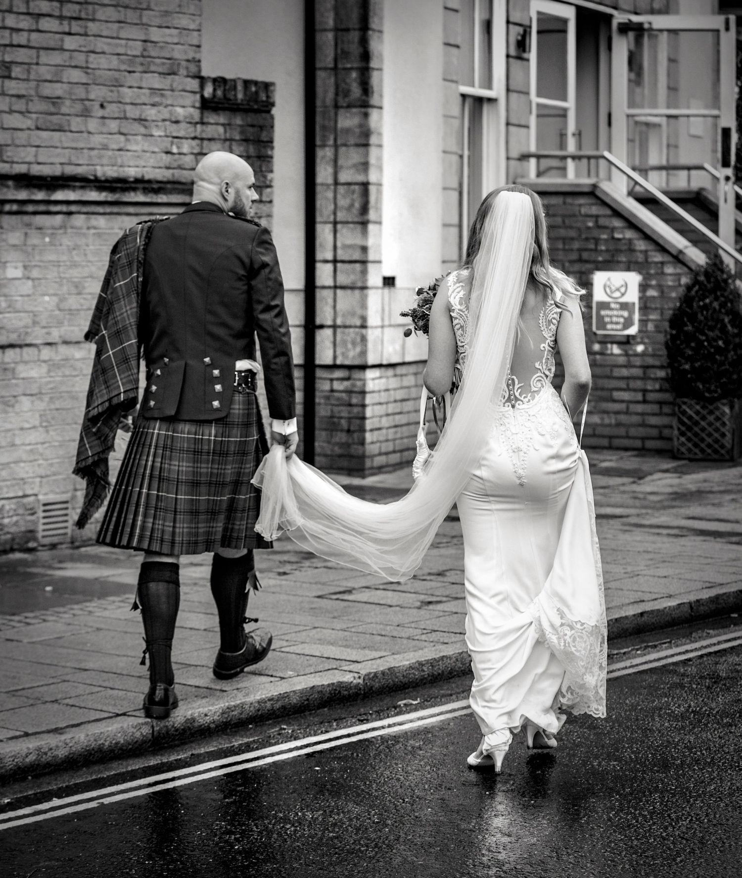 Black and white wedding photos showing a couple walking on a rainy street with a flowing white dress.