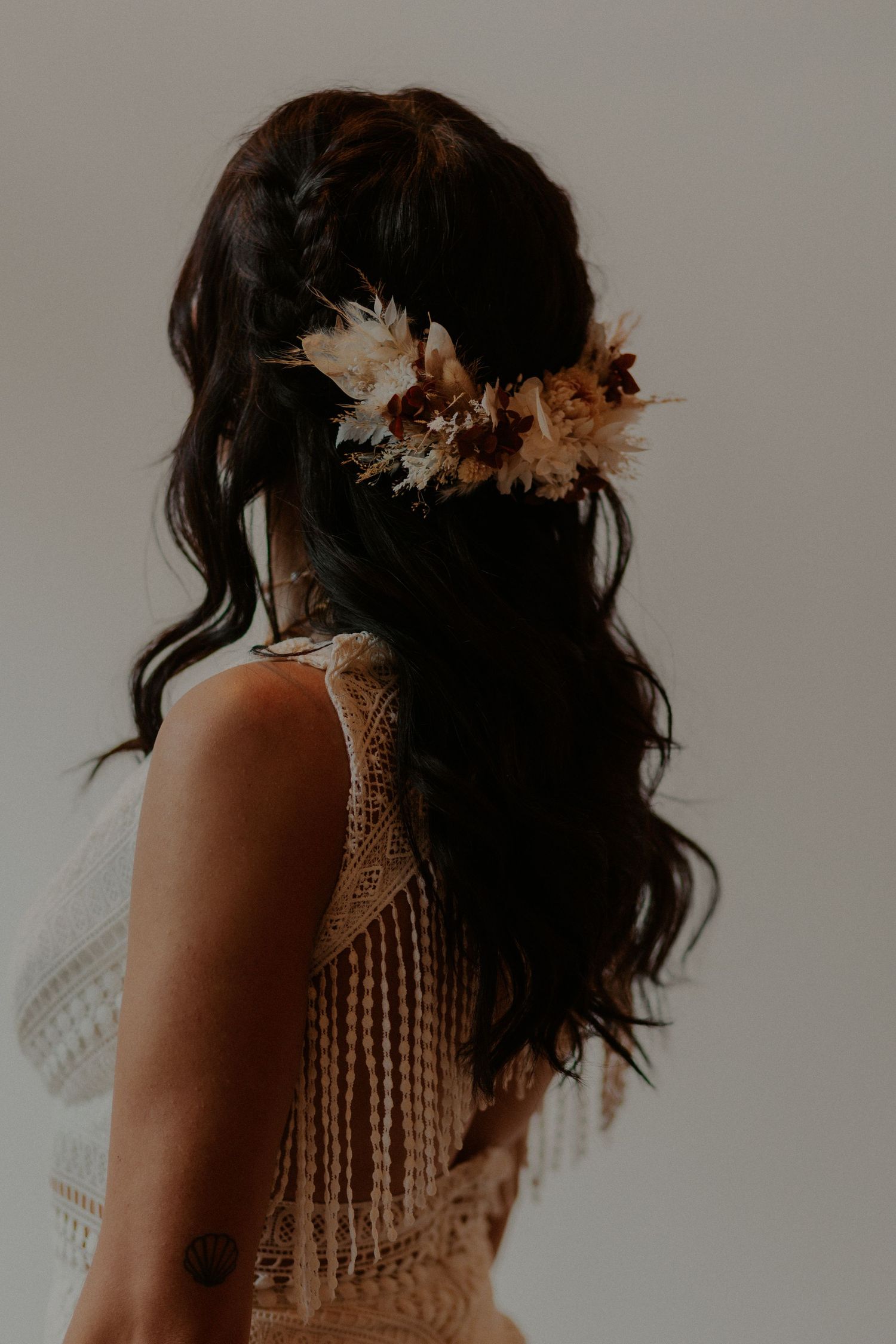 Back view of bridal hairstyle with dried floral hairpiece and flowing dark waves.