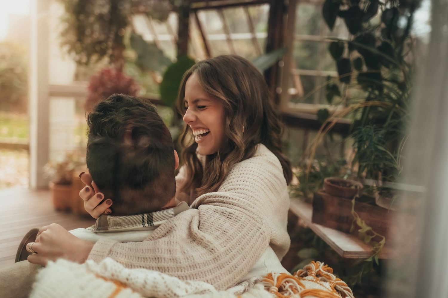 woman and man sitting on chair together laughing through window of greenhouse