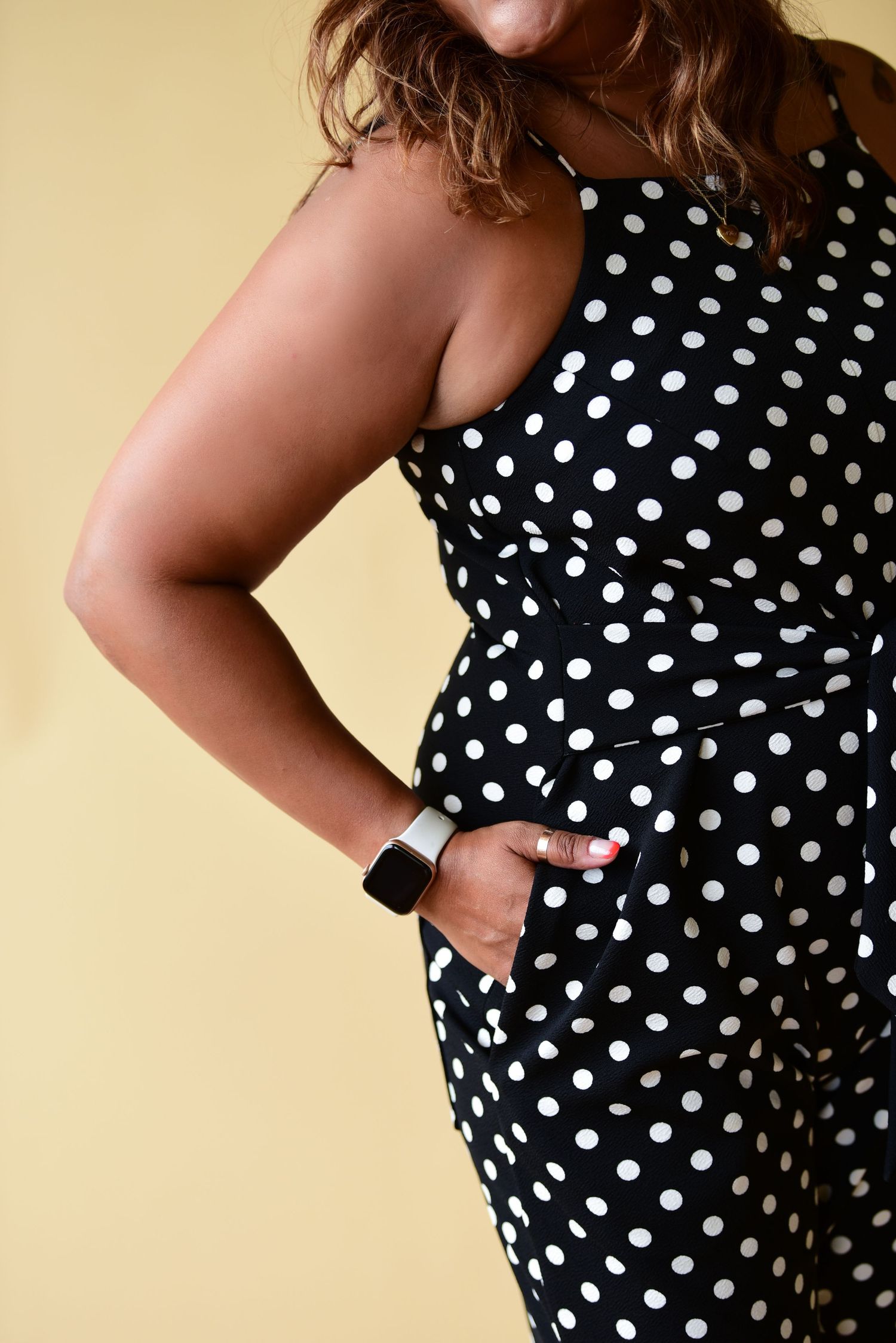 Detail shot of black and white polka dot jumpsuit showing pocket detail and smart watch accessory.