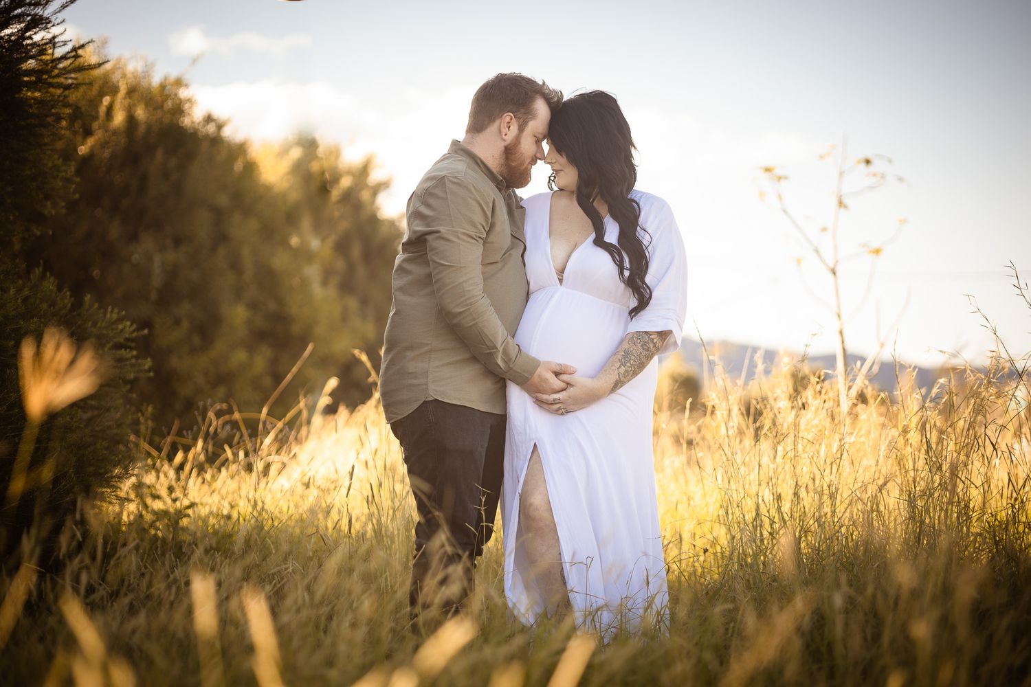 Expecting couple shares a tender kiss in a golden sunset maternity photo outdoors.