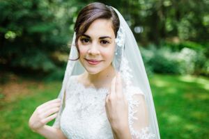 A bride in a delicate lace wedding dress and veil poses in a garden setting.