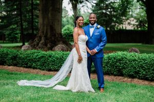 A wedding couple poses formally in a garden setting, with the bride in white and groom in bright blue.