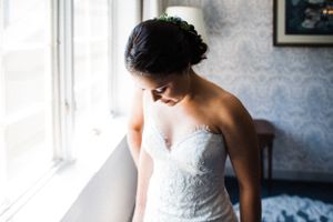 An elegant strapless lace wedding gown is showcased near a window in soft natural light.
