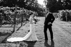 A wedding couple shares a joyful moment in a sun-dappled vineyard with elegant wedding attire.