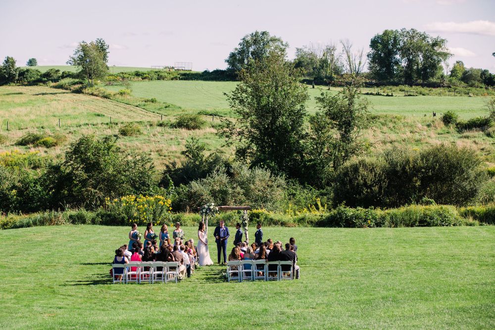 Intimate outdoor wedding ceremony setup in a lush green meadow with rolling hills in the background.