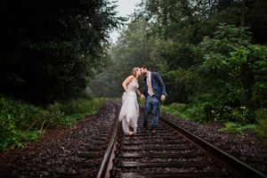 A couple walks together along misty railroad tracks surrounded by green foliage.