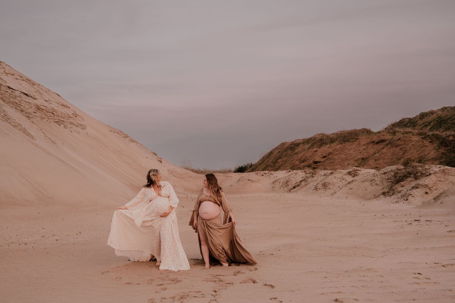 Two people sitting on sand dunes at sunset in warm tones.