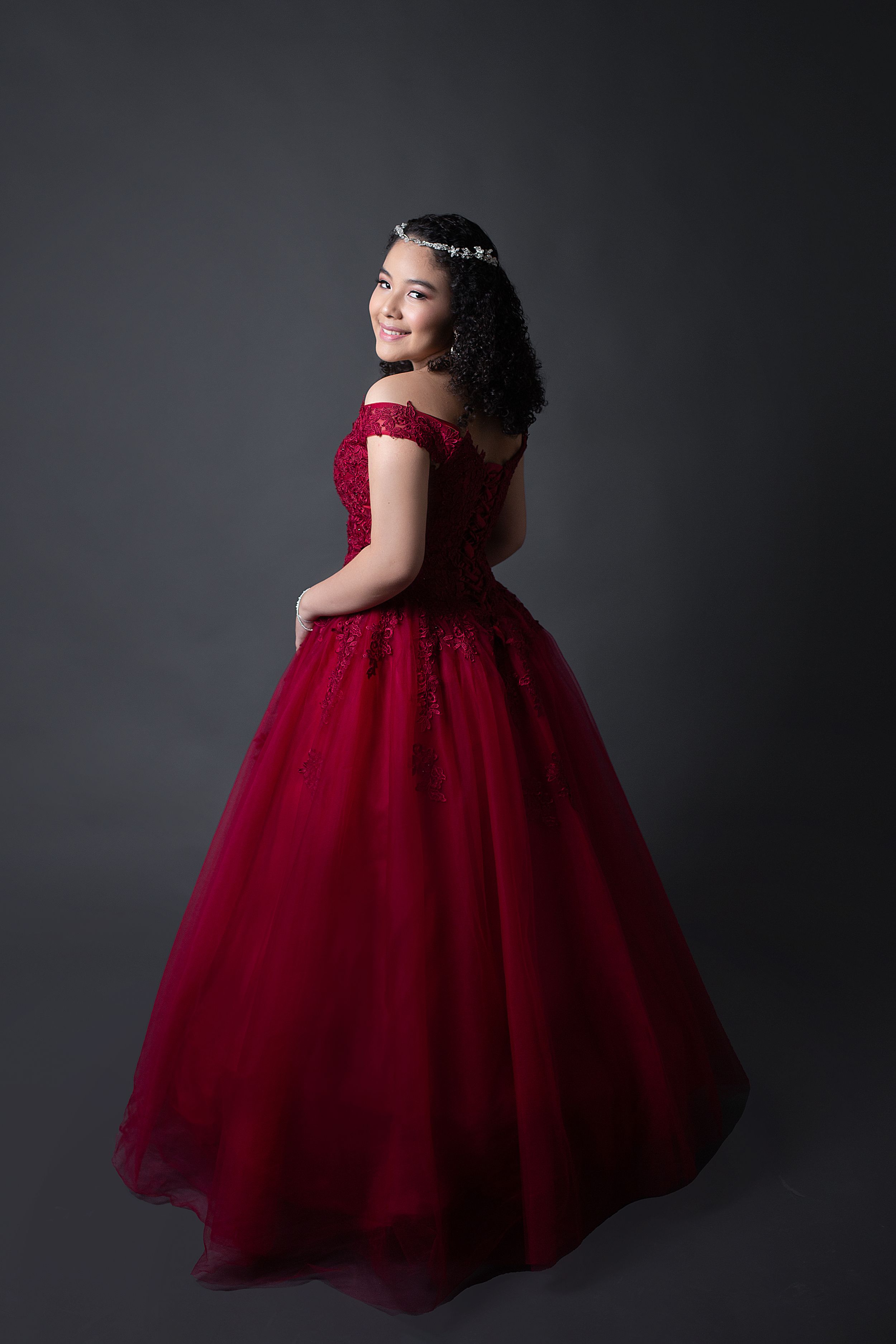 Elegant portrait series of person in flowing burgundy ballgown against dark background.