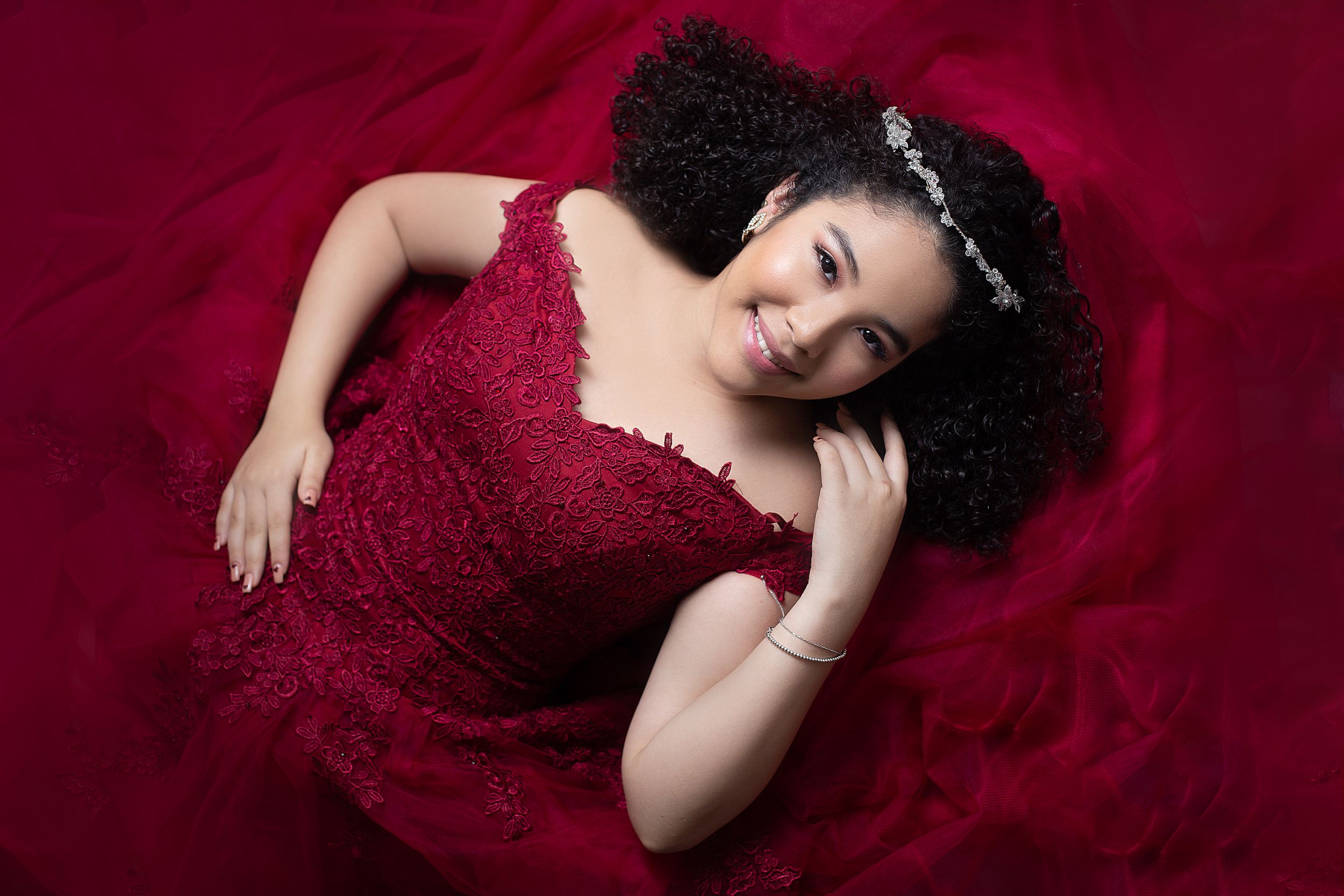 Dramatic photo series of person in deep red formal gown laying on burgundy backdrop.