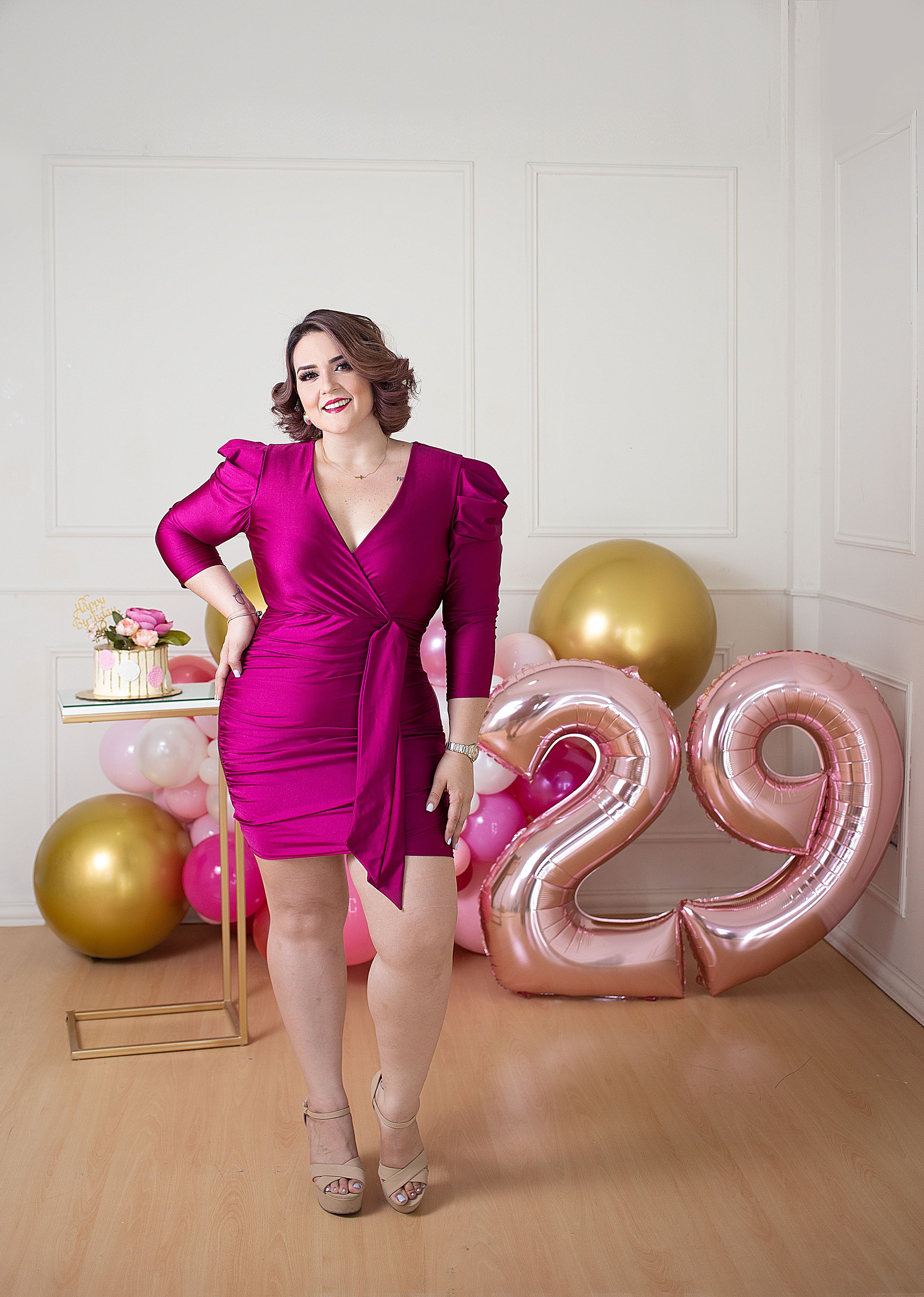 Birthday portrait series with person in magenta dress posing with rose gold number balloons.