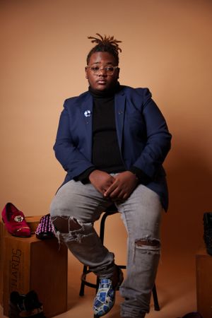 Studio portrait series showing person in navy blazer sitting on boxes against warm background.