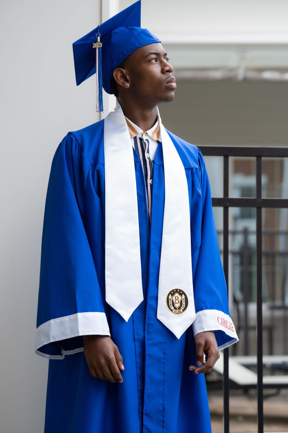 A graduate in royal blue commencement regalia with white stole and honors medallion.