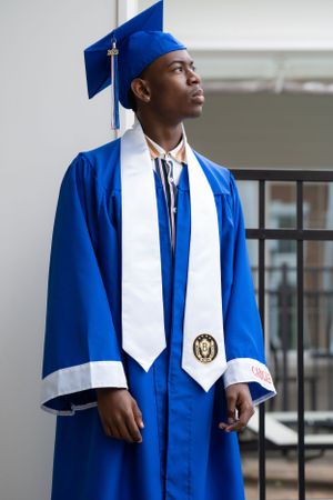 A graduate in royal blue commencement regalia with white stole and honors medallion.