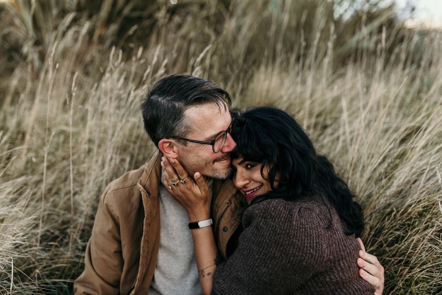 Intimate couple embracing in field of tall grass during golden hour.