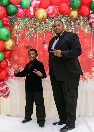 A festive holiday photo setup with red and green balloons, Christmas decorations and two people posing.