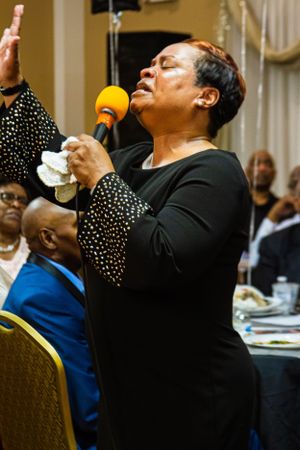A performer sings passionately into a microphone while wearing a black and white polka dot outfit.