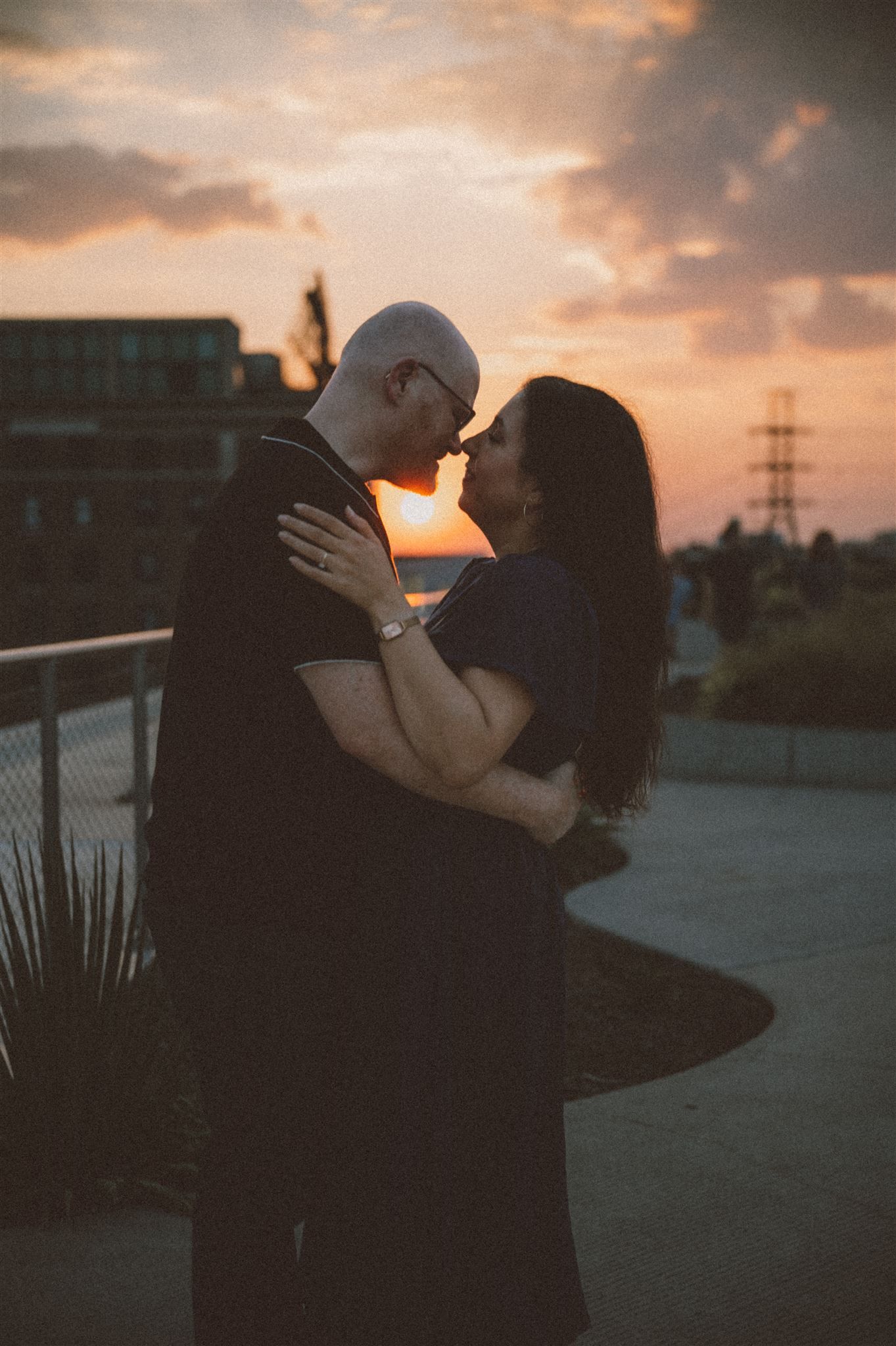 Silhouetted couple sharing an intimate moment at sunset on a city rooftop.
