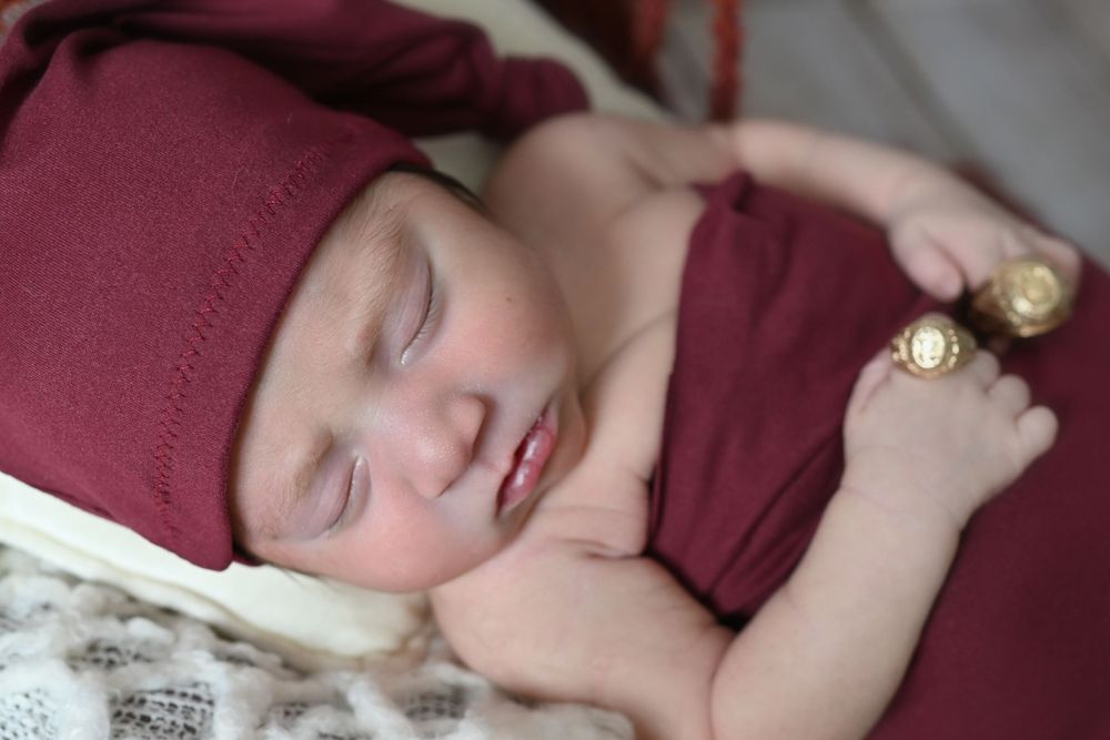 Close-up of a sleeping infant in burgundy clothing with delicate gold accessories.