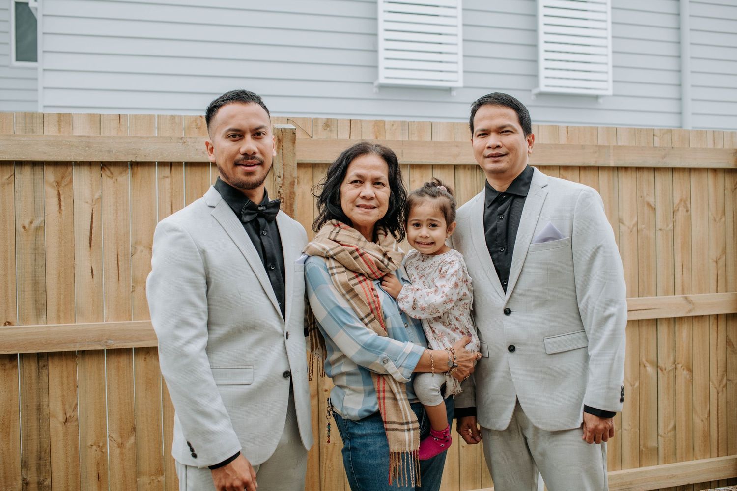 A family group photo in formal attire against a wooden fence backdrop.