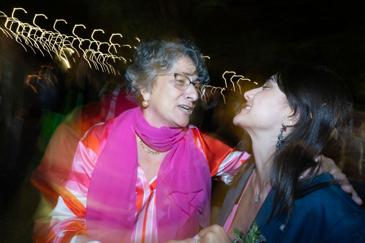 Two party guests share an animated conversation amid blurred light trails at night event.