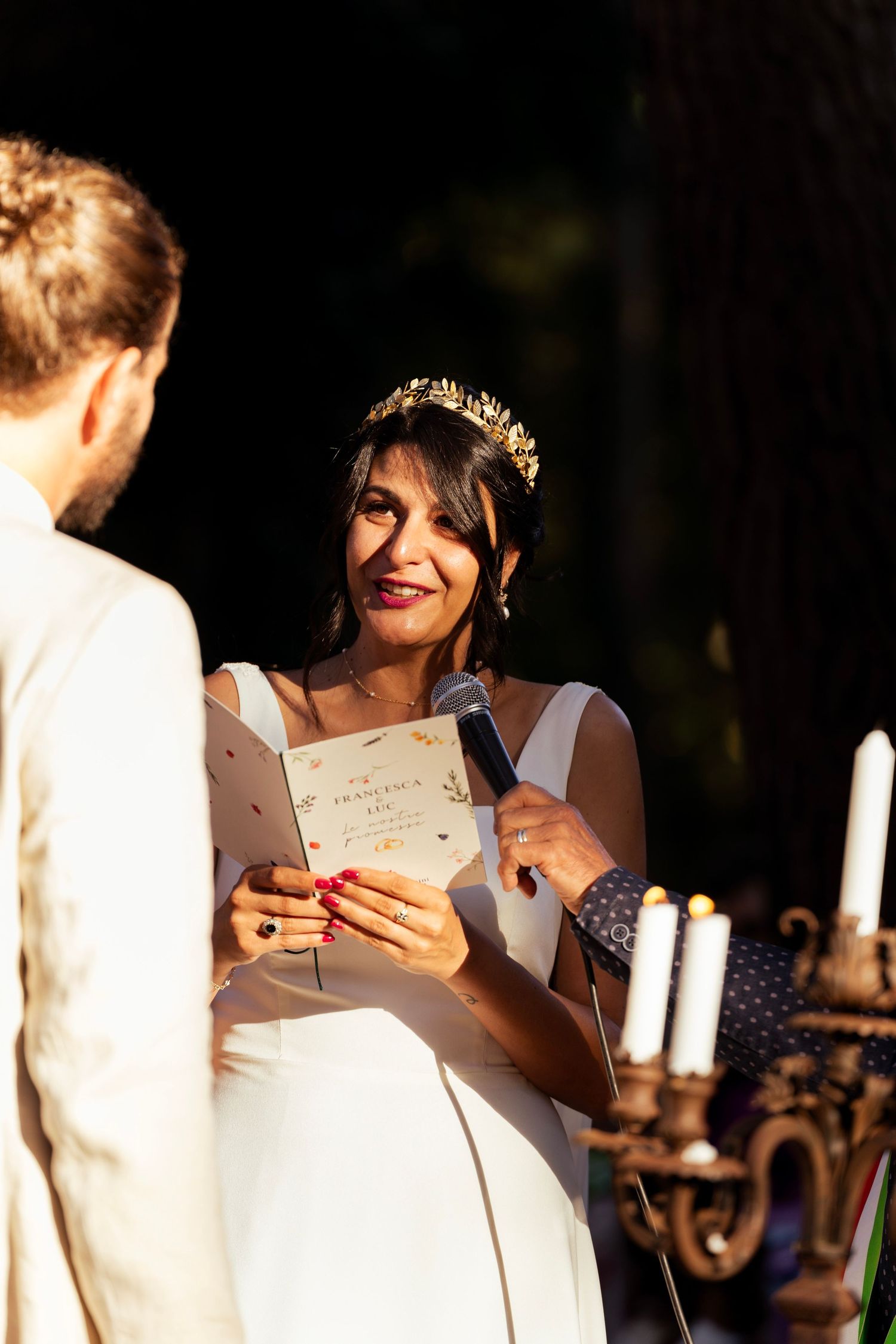 A joyful moment during wedding vow reading in a forest setting with candles.